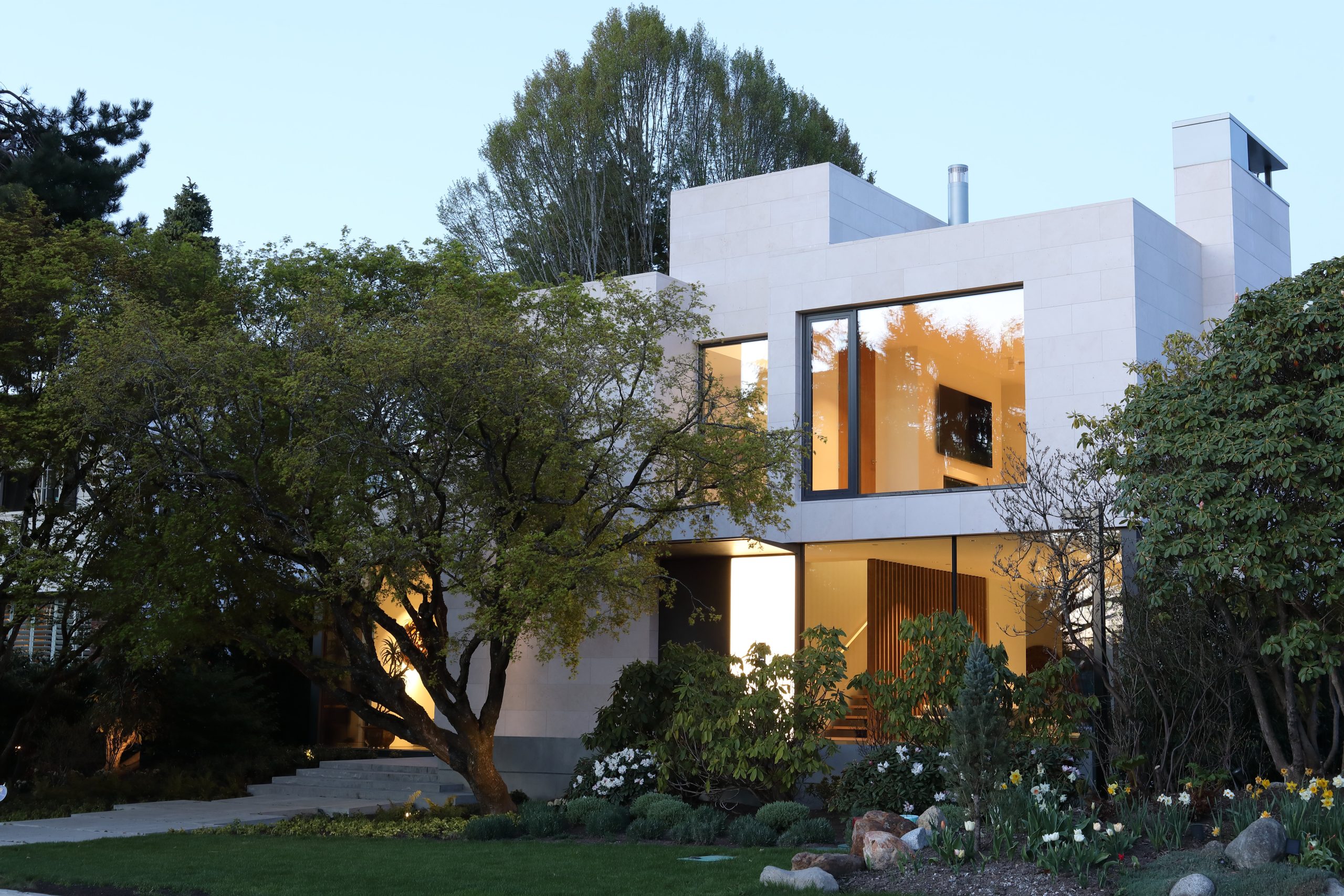 Quality two-story house with large windows, surrounded by trees and a landscaped garden at dusk, showcasing elegant architecture in British Columbia.