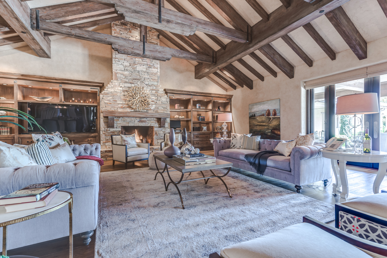 Elegant living room with exposed wooden beams, stone fireplace, plush sofas, and large windows—showcasing timeless British Columbia construction and style.