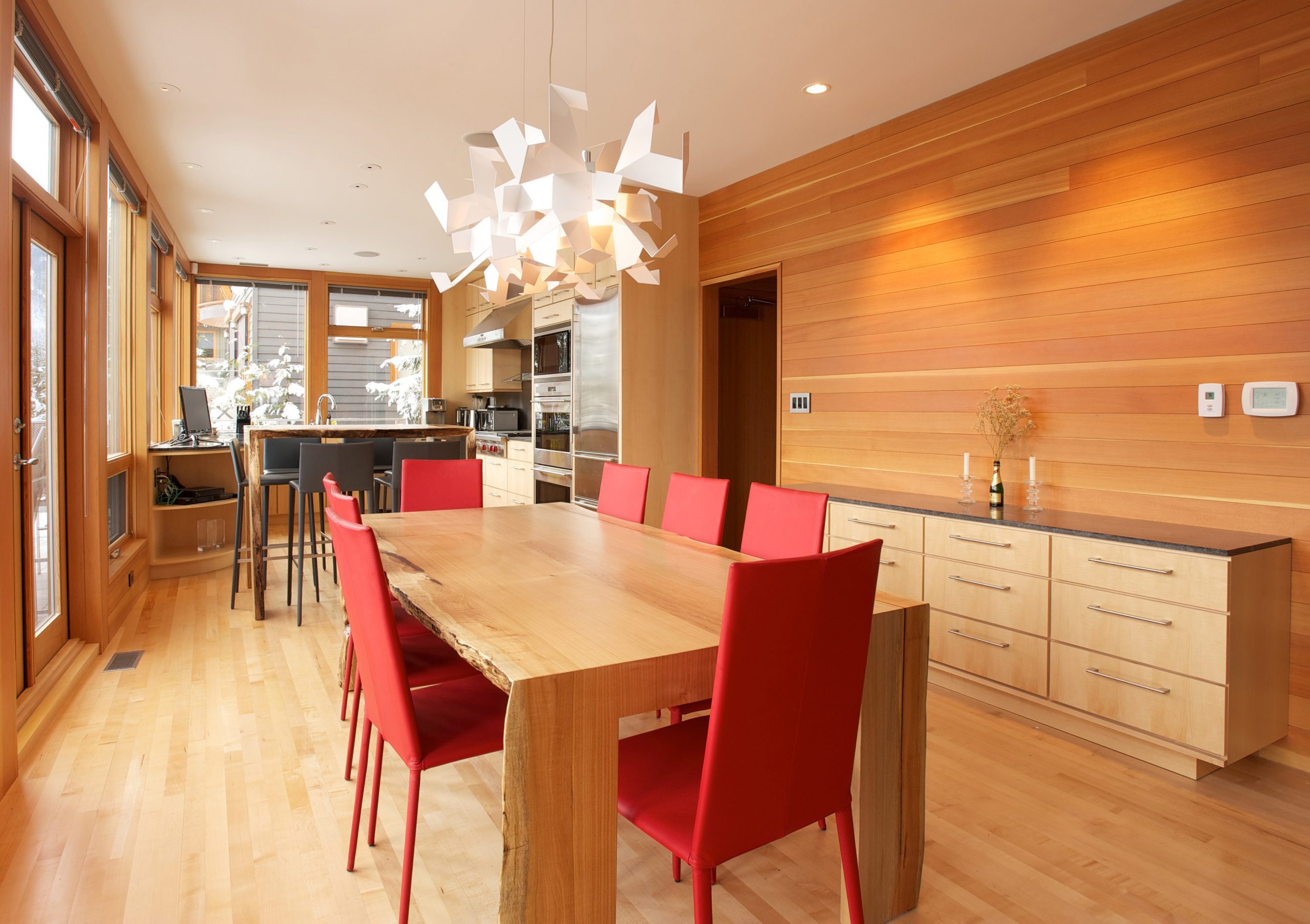 Dining room with a wooden table, red chairs, wood-paneled walls, and a unique white chandelier—perfectly crafted by a skilled general contractor in BC.