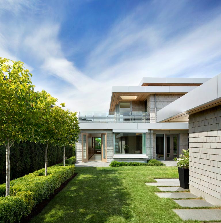 Backyard with green lawn, stone path, and neatly trimmed trees under a blue sky—perfect for contemporary living in Vancouver, British Columbia.