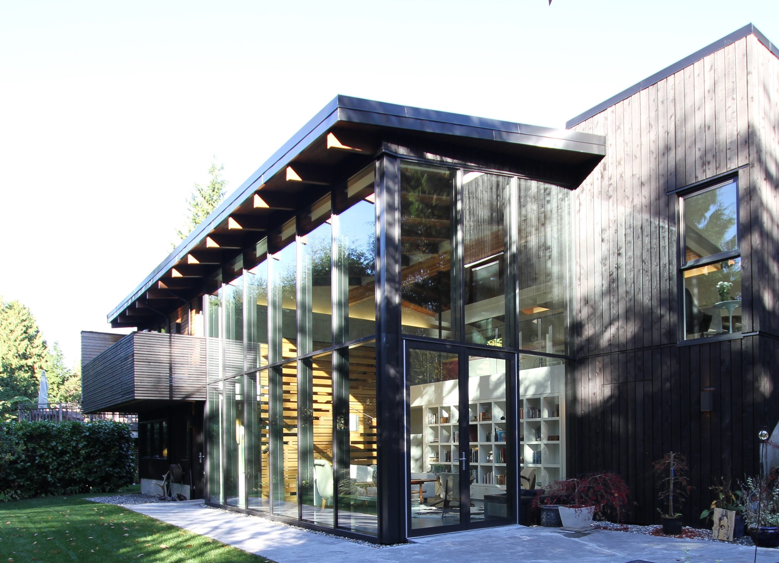 House with large glass windows, dark wood exterior, and a sloped roof, surrounded by greenery—crafted by an expert construction company.