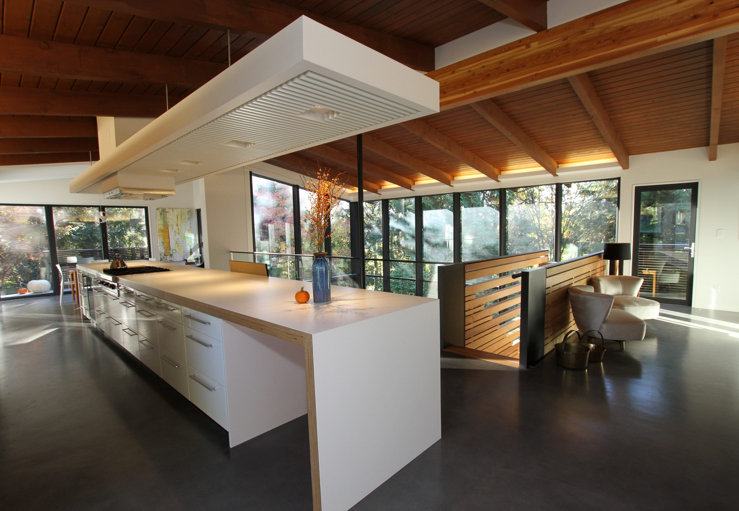 Kitchen by a reputable company in Vancouver, featuring a large island, wooden beams, and floor-to-ceiling windows that flood the space with natural light.