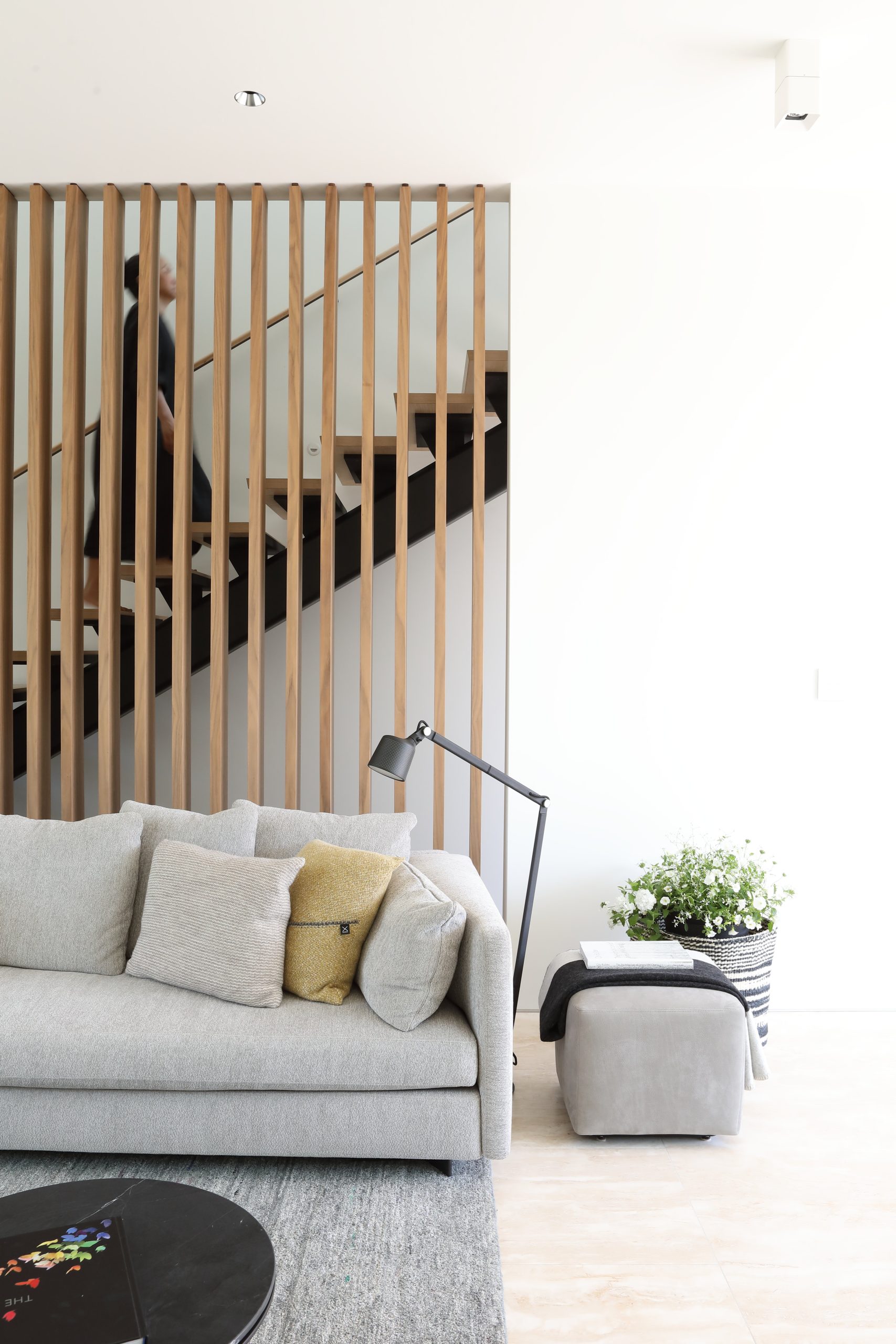 Living room with a gray sofa, floor lamp, and wooden slatted partition by a staircase, showcasing quality architecture inspired by British Columbia design.