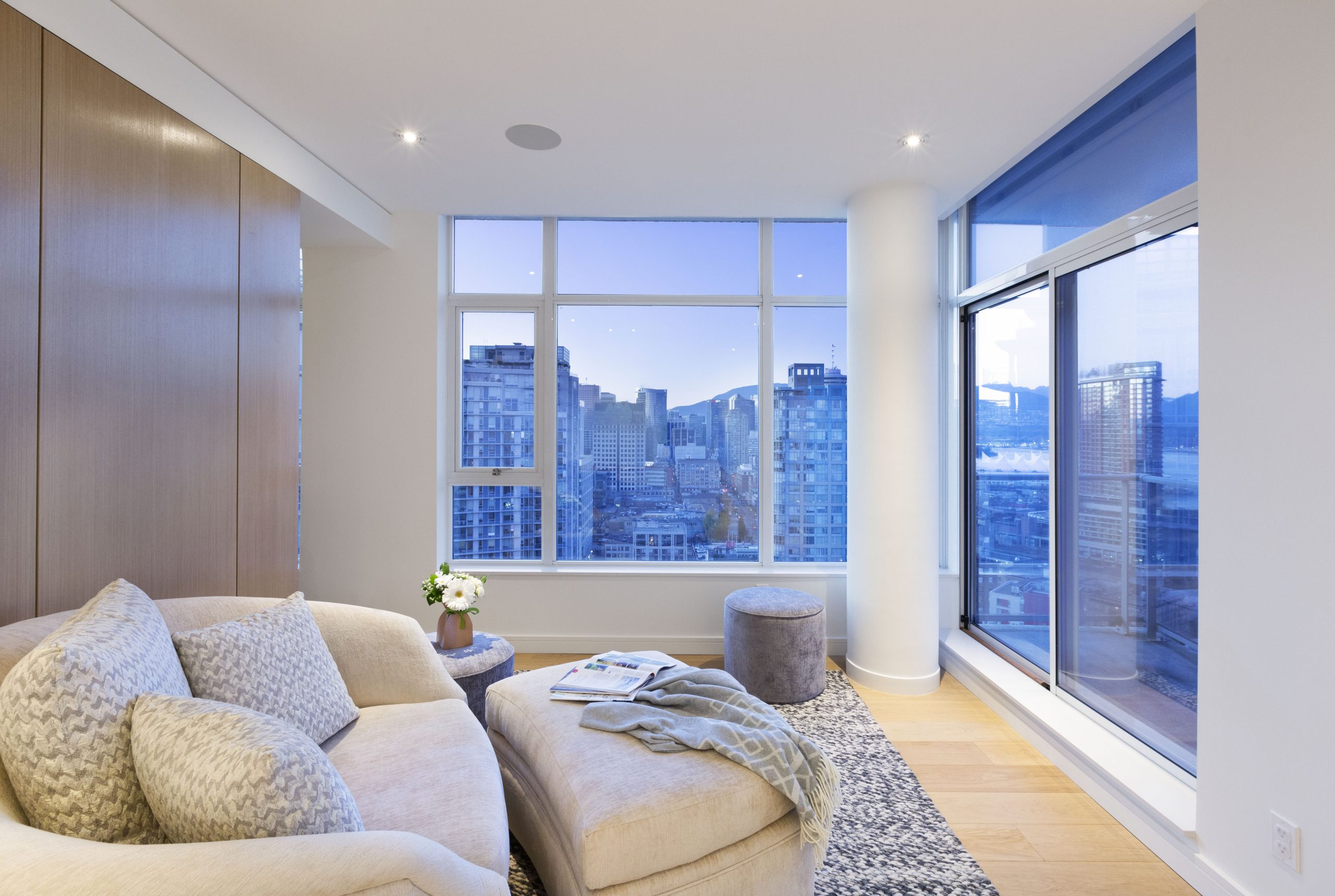 Room with a beige sofa, city skyline views, large windows, and wooden floor—designed by a reputable company known for quality custom homes in Vancouver
